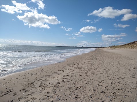 Brittas bay showing blue sky with sparse fluffy white clouds, waves and an empty beach in the sunshine